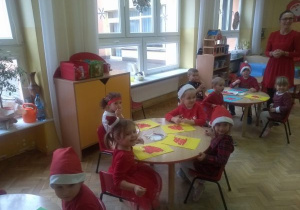 dzieci z gr VIII wyklejają kolorowym papierem czapki Mikołaja